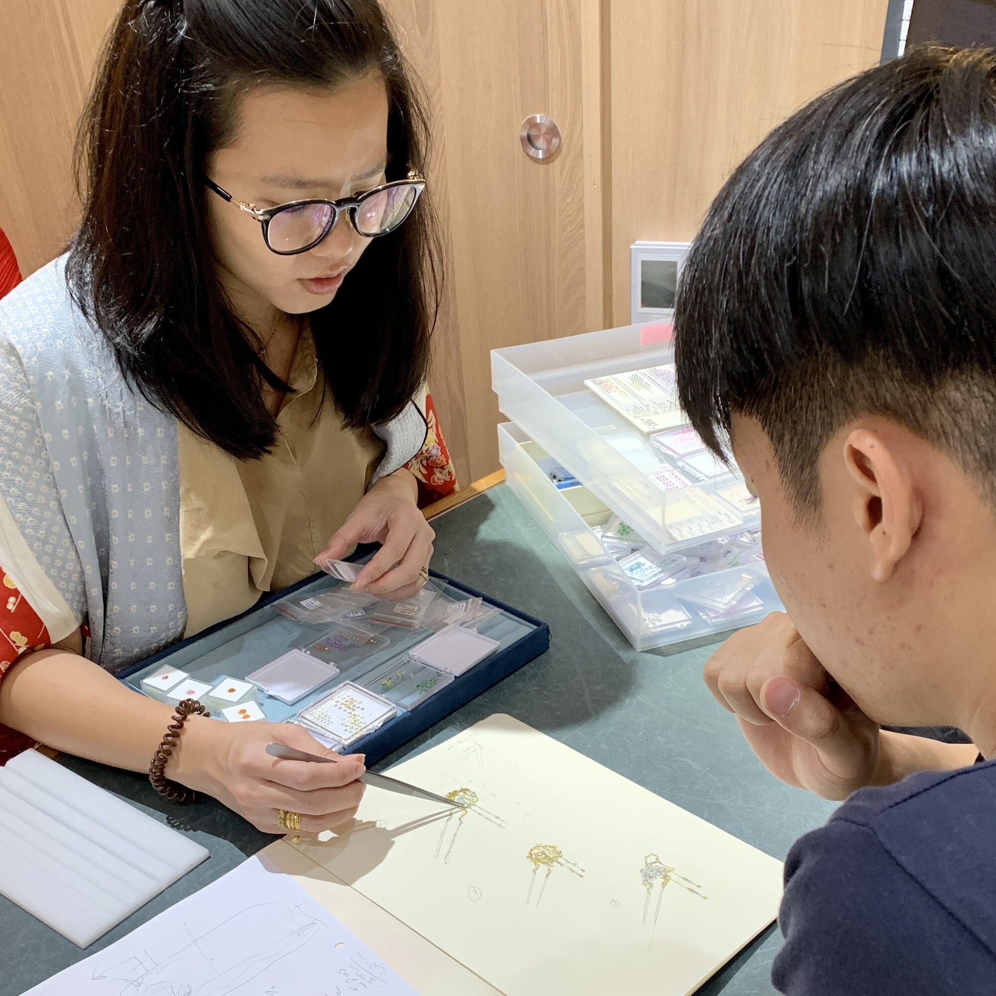 Jewellery consultant discussing gemstone ring design with customer, showcasing gemstone jewellery selection in Singapore boutique showroom.