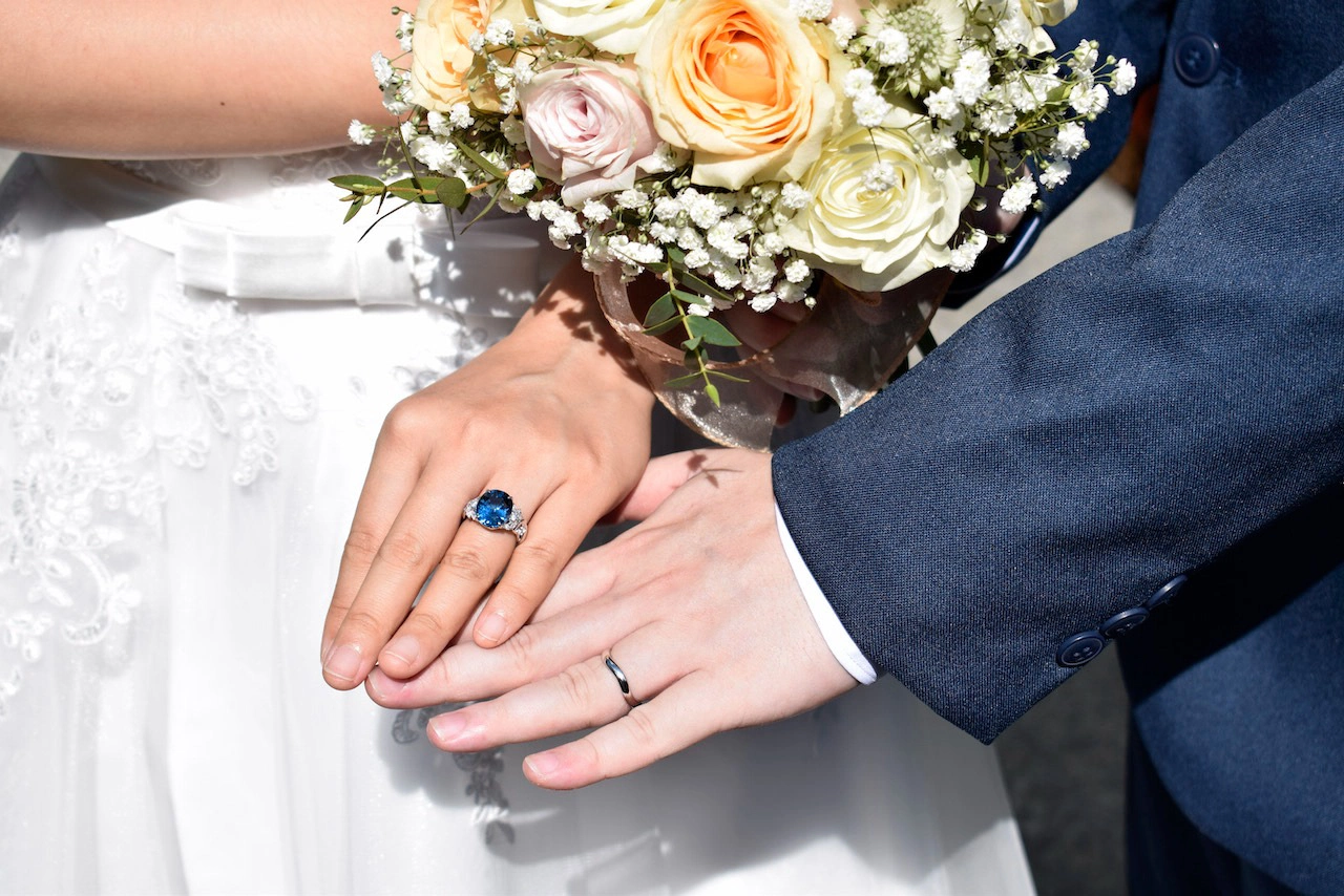 Close-up of bride wearing gemstone ring while holding groom’s arm, symbolising customised wedding ring designs popular in Singapore.